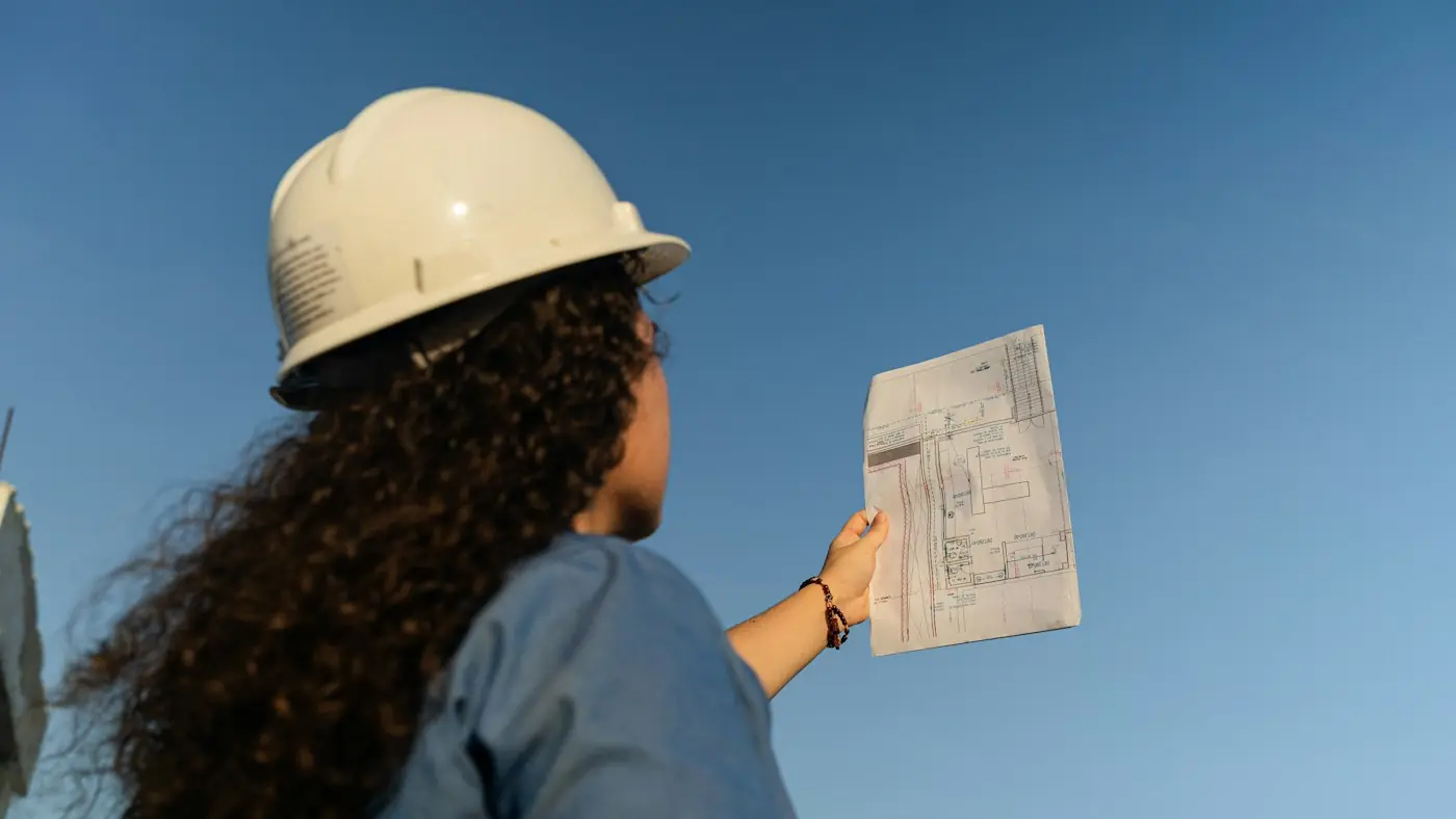 Tecnica di cantiere con casco che consulta i disegni